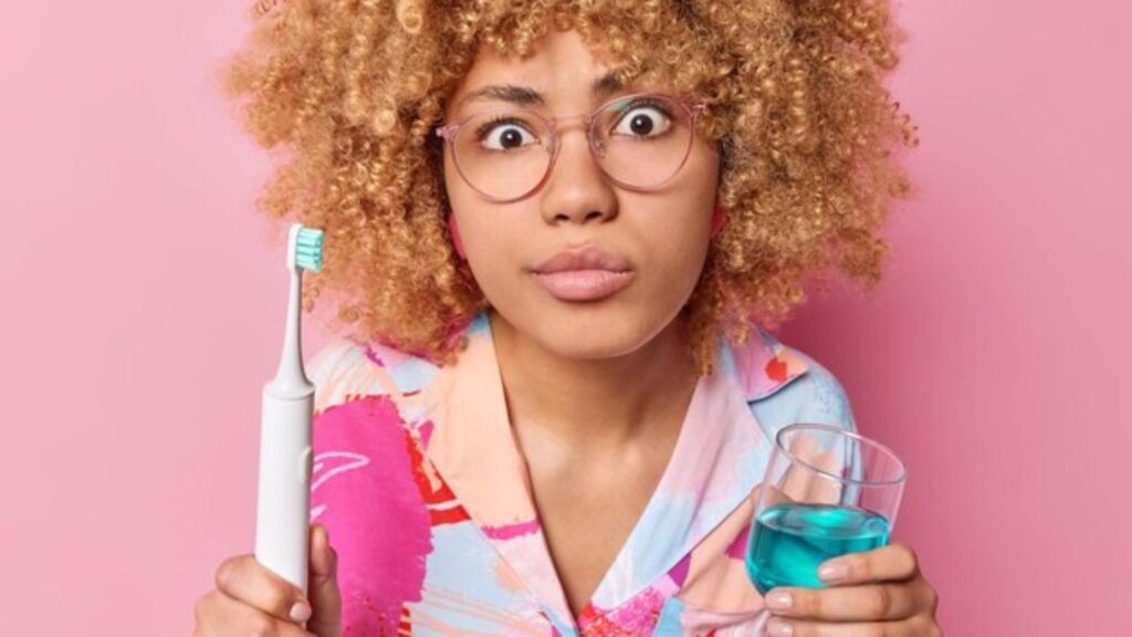 A woman holding a toothbrush and mouthwash, illustrating an essential routine for maintaining fresh breath and oral hygiene