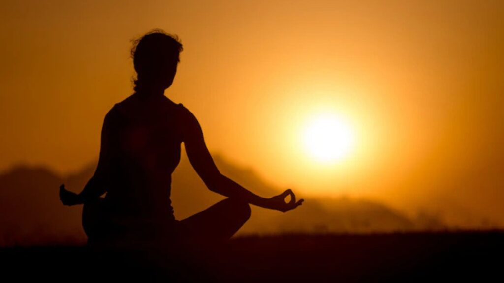 Silhouette of a person meditating at sunrise, creating a peaceful moment to relieve stress.